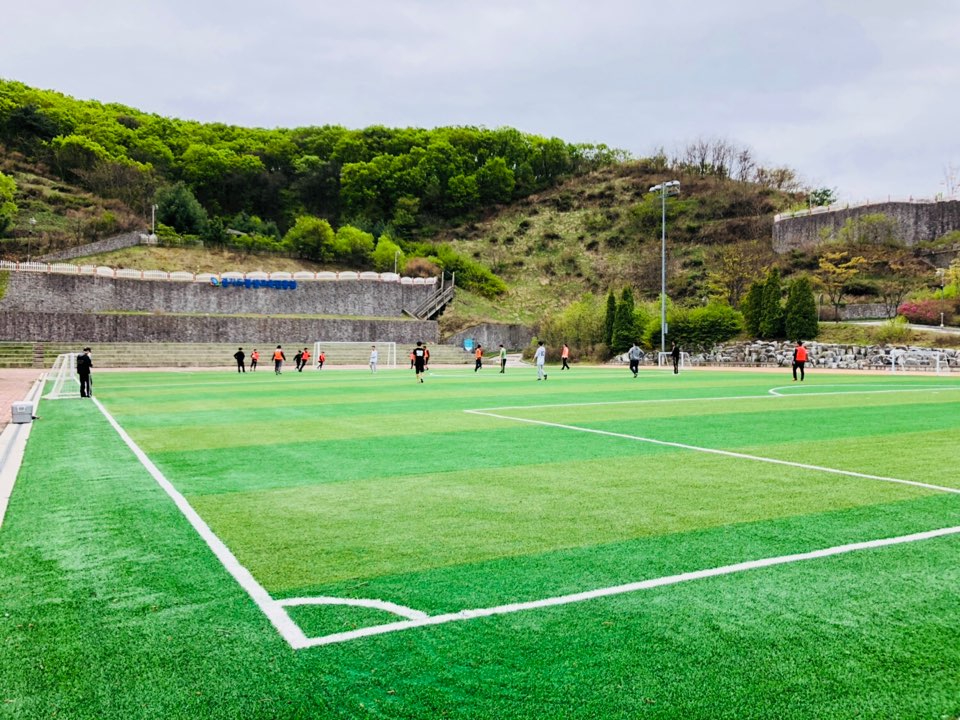 열댓명의 사람들이 먼발치에서 축구하는 모습이 담긴 야외 잔디구장 사진