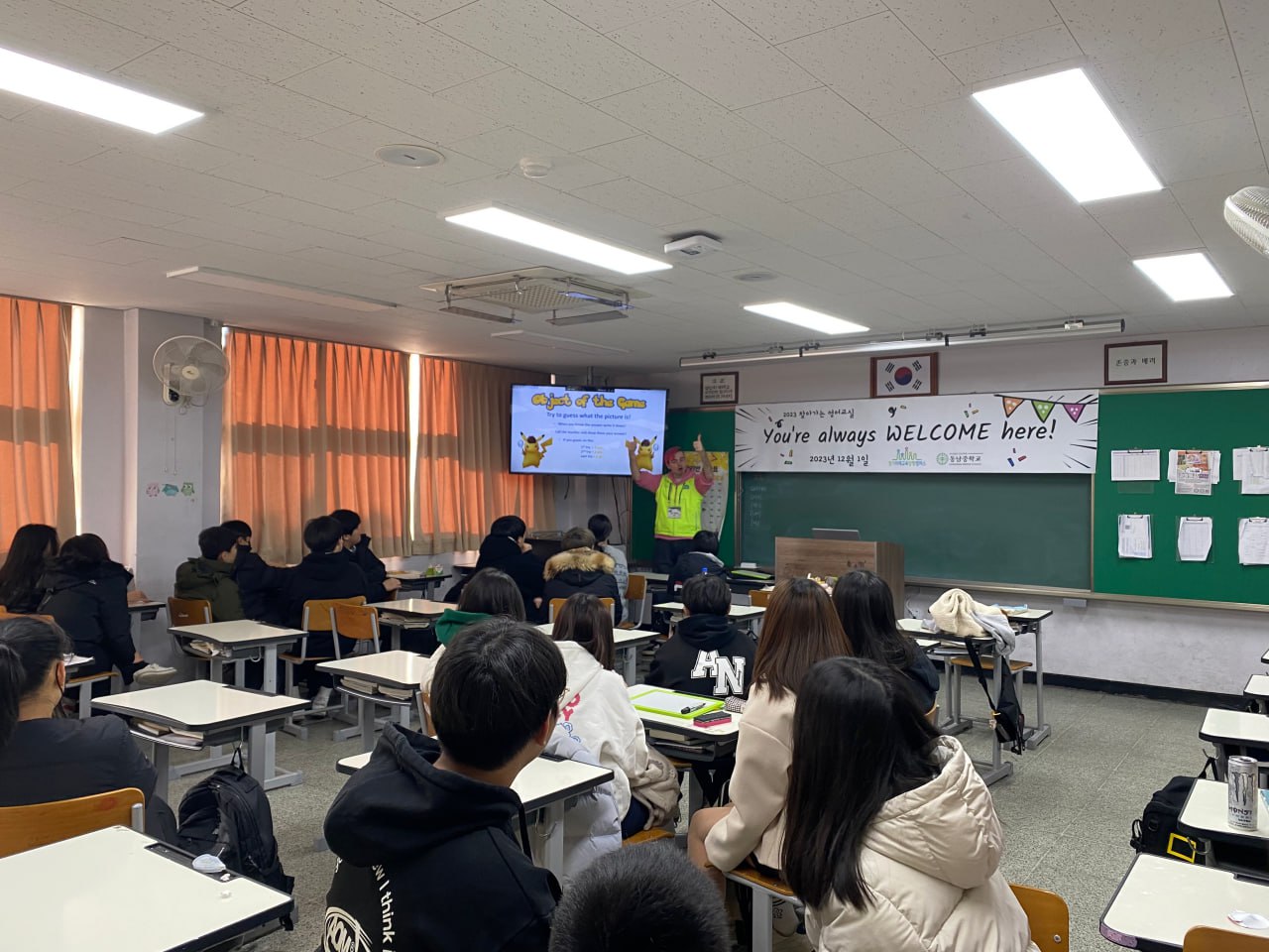 교실에서 영어 수업을 듣고 있는 학생들 교실 한쪽 모퉁이에는 벽걸이 TV가 걸려있으며 영어 수업 자료가 띄워져있다.